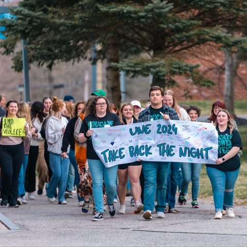 A group of students marches on campus holding a sign that reads "51Ʒ2024 Take Back the Night"